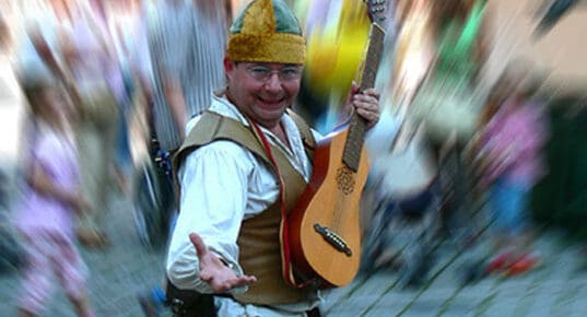A fun busker smiles at the camera with a guitar