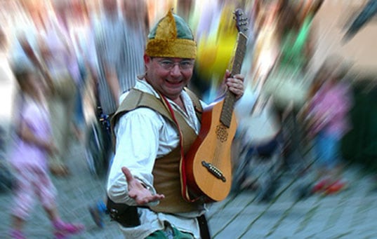 A fun busker smiles at the camera with a guitar