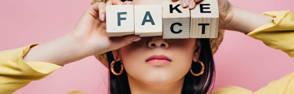 A woman holds letter blocks that spell both "fake" and "fact"