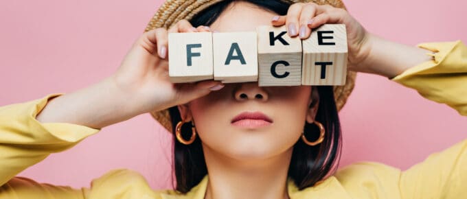 A woman holds letter blocks that spell both "fake" and "fact"
