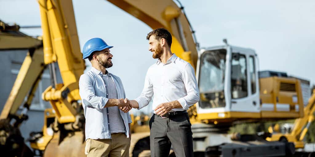 Heavy equipment salesman closing a deal with a man standing in front of a dirt mover. 