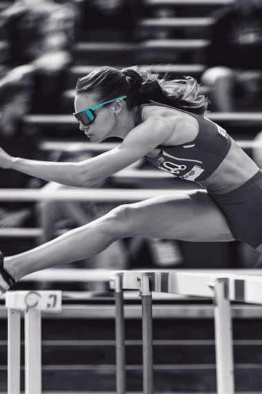 a female athlete in mid-air, leaping effortlessly over a hurdle